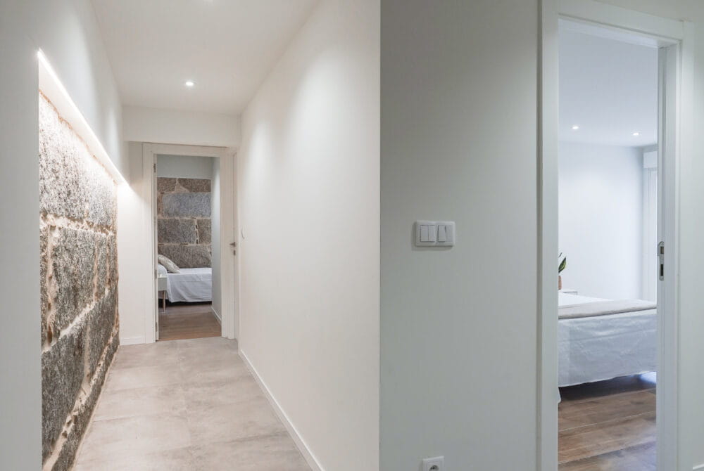 Pasillo moderno con pared de piedra y puerta abierta, conduce a un dormitorio iluminado. Diseño interior minimalista.