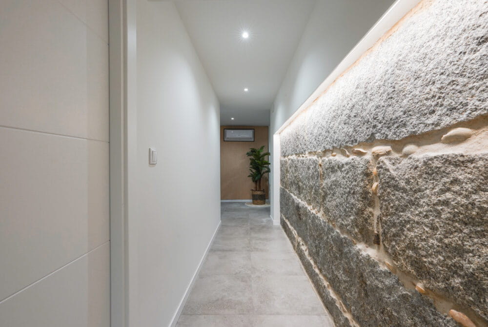 Pasillo moderno con pared de piedra iluminada y planta al fondo, diseño minimalista y acogedor.