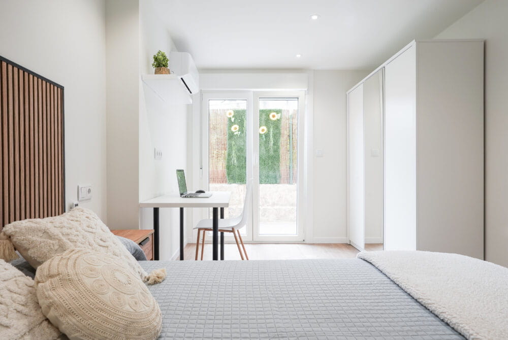 Dormitorio moderno con cama, escritorio y luz natural. Estilo minimalista y acogedor con ventana grande.