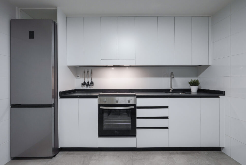 Cocina moderna minimalista con electrodomésticos, estufa, alacenas blancas y encimera negra.